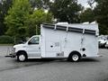 A 2013 Ford Econoline van with a white exterior featuring a side entrance and a raised structure on the roof for equipment storage