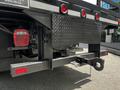 A 2016 Ford F-550 with a dark metallic finish featuring a flatbed design and a diamond plate rear bumper equipped with taillights and a tow hitch