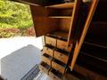 A wooden interior storage unit with multiple drawers and shelves shown inside a vehicle's cargo area