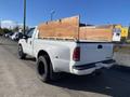 A white 2000 Ford F-350 SD truck with a wooden bed cover and large black tires parked on a gravel road