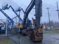 A 2014 John Deere 350G excavator with a large bucket attachment, parked in an industrial area with surrounding machinery and equipment