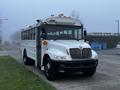 A 2016 International 4200 bus with a white exterior and a large front windshield featuring orange lights on the roof and step at the side for entry