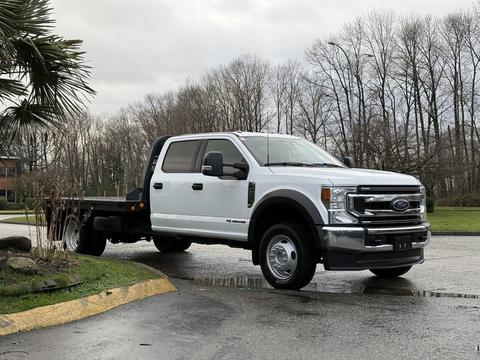 A white 2022 Ford F-550 truck with a flatbed and dual rear wheels is parked at an angle, showcasing its large front grille and side profile