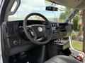 The interior of a 2017 Chevrolet Express featuring a black steering wheel dashboard controls and gear shift with various buttons and a small display screen