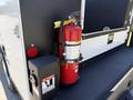 A red fire extinguisher mounted on a black surface with safety labels and a danger sign