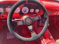 A red 1962 Ford F-100 interior showing a sleek steering wheel with a central logo and multiple gauges in the dashboard