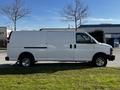 A white 2015 Chevrolet Express van with a boxy shape and large side mirrors parked on grass with shiny wheels and no visible side windows