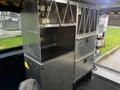 A silver metal storage unit installed inside a 2020 Ford Transit with shelves and drawers designed for organizing equipment and tools