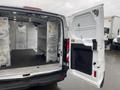 A 2018 Ford Transit van with open rear doors revealing an empty cargo area lined with metal shelving and a partition