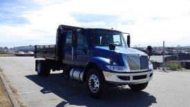 A blue 2012 International DuraStar 4300 truck with a flatbed and chrome front grille parked on a street