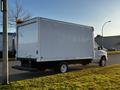 A 2017 Ford Econoline box truck with a white exterior parked on the street showing its rear side and a single orange light on the roof