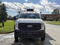 A white 2024 Ford F-550 truck with a black grille and bumper facing forward featuring side mirrors and a roof-mounted light bar