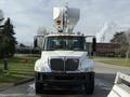 A white 2011 International 4300 truck with a bucket lift attached at the front facing the viewer