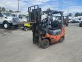A 2010 Toyota 7FGGU25 forklift with an orange and black exterior featuring a raised fork attachment and a driver's seat visible in the cabin