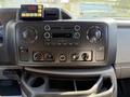 Dashboard of a 2011 Ford Econoline featuring a radio system with knobs and buttons along with a display screen and a storage compartment