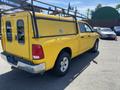 A yellow 2015 RAM 1500 pickup truck with a tool rack and a truck bed cover parked in a lot