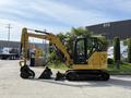 A yellow 2022 Caterpillar 306 excavator with a retractable arm and large digging bucket parked on a surface with low vegetation nearby