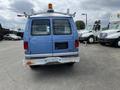 A blue 2009 Ford Econoline van with a rusty rear bumper and a roof rack featuring an orange light on top