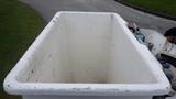 A large white plastic bin mounted on a truck used for waste collection with visible wear and dirt on the surface