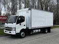 A 2018 Hino 195 truck with a white box cargo body and a black chassis parked on a driveway
