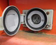 An open electrical outlet with a round shape and three prongs, mounted on a metal surface