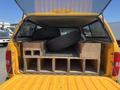 The back of a yellow Chevrolet Silverado 1500 shows two stacked tires resting on wooden structures with several compartments