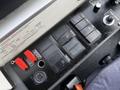 A control panel featuring several switches buttons and indicators in a vehicle cockpit with a red emergency stop button and a power outlet on the side