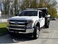 A 2021 Ford F-550 in white with a flatbed attached, showcasing a large front grille and chrome accents, parked on a street