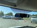 View through the front windshield of a vehicle showing a rearview mirror and a parking lot filled with various trucks and vans including a 2012 GMC Savana