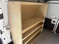 A wooden shelving unit with three open shelves inside the cargo area of a van