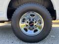 A close-up of a chrome wheel rim on a 2019 GMC Savana featuring five circular holes and a red GMC logo in the center mounted on a rugged tire