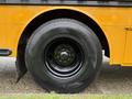 A close-up of a black tire on a yellow school bus showing the tread and rim details