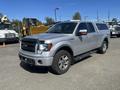 A 2014 Ford F-150 in silver with a black grille and chrome accents parked at an outdoor location with a cap on the truck bed and all-terrain tires