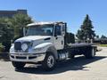 A 2018 International DuraStar flatbed truck with a silver and white exterior featuring a prominent front grille and multiple cargo straps on the bed