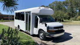 A white 2011 Chevrolet Express shuttle bus is parked with its doors open and front visible showcasing a large windshield and chrome grille