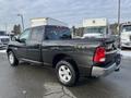 A 2015 RAM 1500 pickup truck with a black exterior and silver wheels parked on a wet surface showing the rear and side profiles