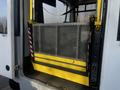 A yellow and black wheelchair lift with a metal grid design is partially lowered at the back of a vehicle marked as a 2018 Chevrolet Express