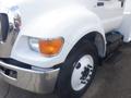 A white 2011 Ford F-750 truck with a distinctive front grille and large tire showing a black step near the rear wheel arch