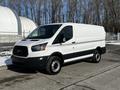 A white 2018 Ford Transit van with black trim and a sliding side door parked on a paved surface