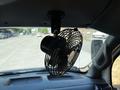 A small black oscillating fan mounted on the ceiling of a vehicle's interior