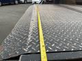 A close-up of a scratched metal surface with a measuring tape laid across it on a truck bed