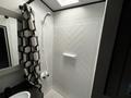A modern shower stall featuring a herringbone patterned white tile design with a built-in shelf and a black and white geometric shower curtain