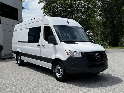 A 2019 Mercedes-Benz Sprinter van in white with a black front grille and wheels parked at an angle with a sleek design and large windows