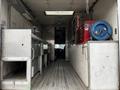 Interior of a 2006 GMC C5000 showing metal work tables a tool chest and a blue hose reel along the wall