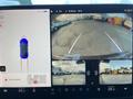 A 2019 Tesla Model 3 is displayed on a car screen with a rear camera view showing parking lines and surrounding vehicles including trucks