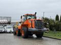 A 2018 Doosan DL300-5 construction loader in orange color with large tires and a front bucket attachment