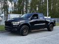 A black 2019 RAM 1500 truck with a crew cab and aftermarket wheels parked on a gravel surface