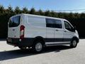 A 2023 Ford Transit van in white with sliding side doors and a rear cargo area visible from the side