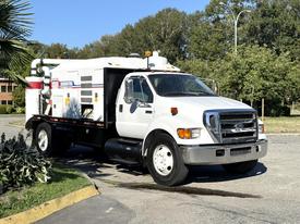 A 2006 Ford F-650 truck with a white body and black flatbed featuring equipment on the rear for industrial use