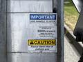 A close-up of a metal lift with safety warning labels including maximum capacity of 3000 pounds and instructions to stand clear of the platform area